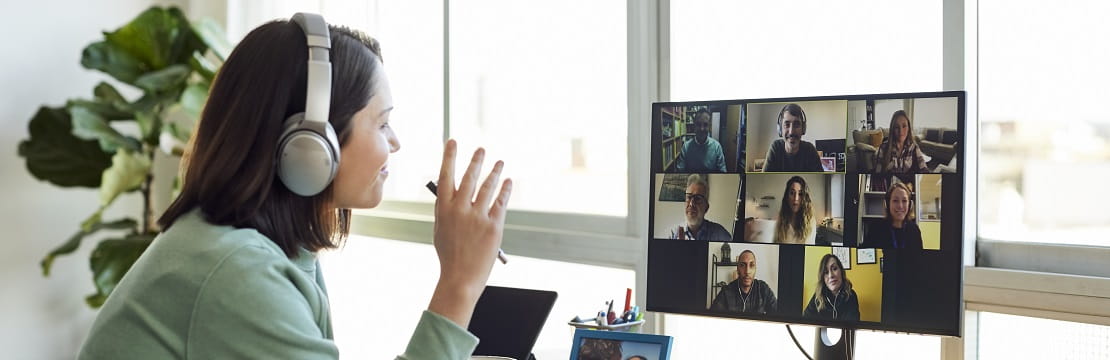 Woman waves to coworkers on a video call at her desk.